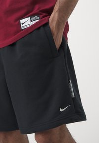 Calções de algodão pretos com uma textura suave, apresentando bolsos laterais, um logótipo da Nike branco e uma etiqueta na cintura com detalhes da marca.
