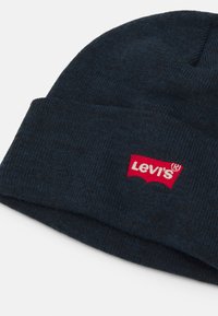 Gorro de punto en azul oscuro, con un parche del logo rojo de Levi's. Textura suave, diseño ajustado con un dobladillo enrollado para mayor calidez.