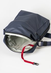 Navy crossbody bag with top zipper open, showing light gray interior and red strap with black clasp inside.