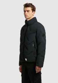 Zwart gewatteerd jack met hoge kraag, ritssluiting, zijzakken met rits en een getextureerd quiltpatroon; voorzien van een rond logo-opschrift op de mouw.