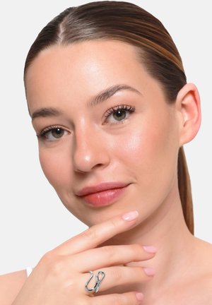 Giovane donna con pelle liscia e trucco leggero che indossa un anello d'argento dalla forma astratta sull'indice vicino al mento.