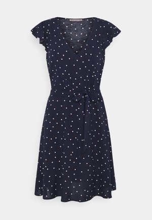 Granatowa sukienka z krótkim rękawem w białe kropki, z dekoltem w serek i wiązaną kokardą w talii, do kolan, z lejącej się tkaniny.