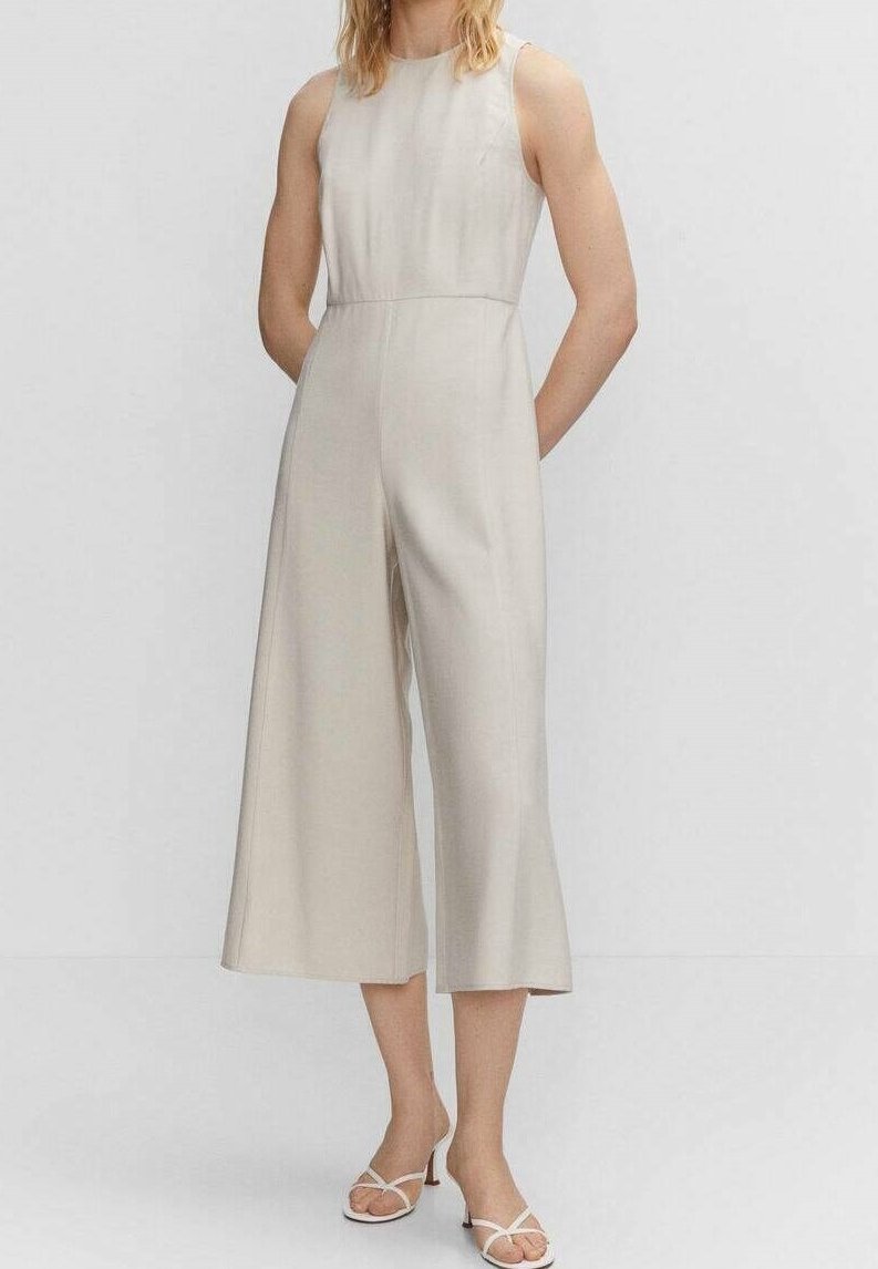 Combinaison large beige sans manches, texture lisse, longueur mi-mollet et coupe ajustée, associée à des sandales blanches à lanières.