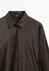 Camicia button-up marrone a maniche lunghe realizzata in tessuto liscio. Presenta un colletto classico e cinque bottoni, con un design elegante e minimalista.