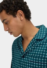 Tričková košile na spaní s tyrkysovým vzorem a kruhovými motivy, vybavená límečkem, zapínáním na knoflíky a kontrastním tmavě modrým lemem. Tkanina vypadá měkce.