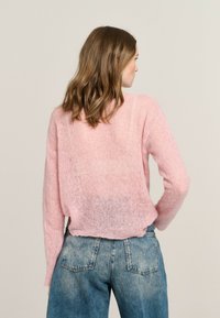 Helles rosa, verkürztes Sweater mit weichem, strukturiertem Strick, langärmlig und leicht lässig geschnitten, kombiniert mit hochtaillierten Jeans.