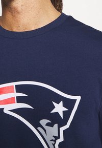T-shirt en coton bleu marine arborant un grand logo blanc et rouge d'une équipe de football, avec un design circulaire et un accent en étoile près du logo.