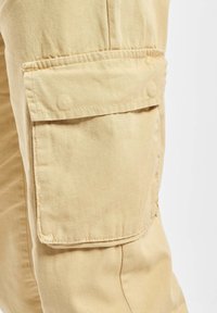 Beige cargobroeken met een zijvak, gemaakt van een lichte stof met een soepele textuur, benadrukkend gebruiksgemak en functionaliteit.