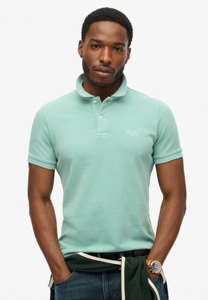 Lys grøn polo skjorte lavet af struktureret stof, med krave og to-knaps placket. Diskret logo på brystet, parret med mørke jeans.
