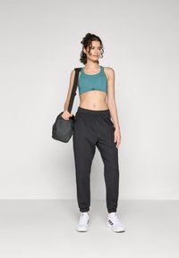 Tyrkis sport-BH, svarte joggebukser med elastisk midje, hvite sneakers. Svart skulderveske. Rett passform, glatt stoff, avslappet design.