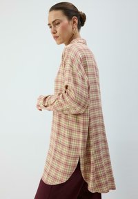 Chemise à manches longues avec boutons, motif à carreaux rose et crème, dotée d'une coupe décontractée et de fentes sur les côtés. Confectionnée en tissu léger.