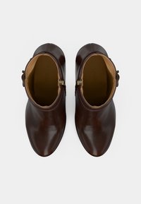 Δίδυμο καφέ δερμάτινα μποτάκια μέχρι τον αστράγαλο με πλαϊνές αγκράφες, με θέα από πάνω σε λευκό φόντο.