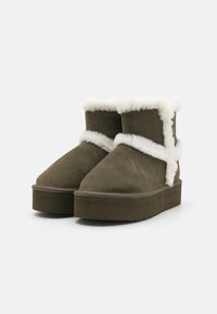 Oliivroheline suede-stiilis põlvepüksid valge vale fliisiga, lameda platvormi tallaga, ümarate varvastega ja õmmeldud aksendiga kingakannu juures.