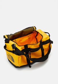 Yellow duffel bag made of durable material. Features black accents, adjustable straps, a mesh pocket, and a large open compartment.