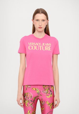 T-shirt di cotone rosa con maniche corte, con la scritta "VERSACE JEANS COUTURE" in bold giallo sul petto.