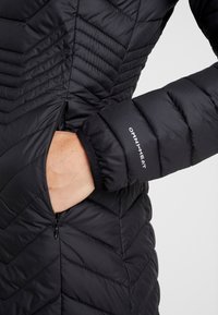 Zwarte donzenjas met chevron-stiksels, een ritssluiting aan de zijkant en "OMNI-HEAT" branding op de manchet, met een gladde, geïsoleerde textuur.