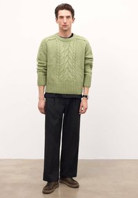 Suéter de punto trenzado verde claro con puños y dobladillo acanalados, combinado con pantalones anchos negros y zapatillas de ante marrón.