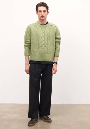 Suéter de punto trenzado verde claro con puños y dobladillo acanalados, combinado con pantalones anchos negros y zapatillas de ante marrón.