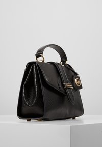 Svart läderhandväska med en texturerad yta, guldfärgade detaljer, ett handtag på toppen och en lockförslutning med en logo-detalj.