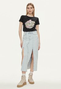 T-shirt in cotone nero con grafica floreale, abbinato a una gonna di jeans azzurra chiara con spacchi laterali e orlo sfrangiato. Stivali da combattimento beige completano il look.