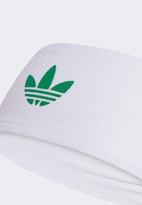 Bijela sportska traka za glavu od teksturirane tkanine, s zelenim Adidas logotipom koji ima tri listolika elementa i horizontalne pruge.