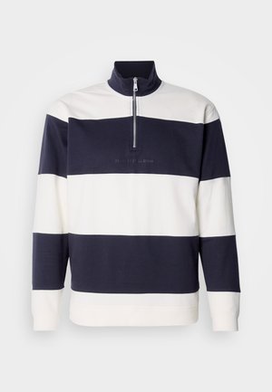 Tengerészkék és fehér csíkos pulóver, magas gallérral és negyed zipzárral. Puha pamut anyag, elöl hímzett logóval.