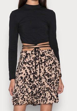Femme portant un crop top noir à manches longues avec liens à nouer et une jupe beige à volants avec imprimé léopard noir.