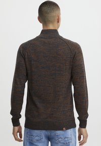 Maglione lavorato a maglia di colore blu scuro e ruggine con colletto alto, polsini e orlo a coste. Presenta un motivo testurizzato e un'etichetta di marca sull'orlo.