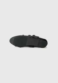 Scarpa in pelle nera con doppia fibbia, mostrata dal basso che mette in evidenza la suola e il tacco in gomma testurizzata.