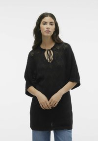 Zwarte gebreide pullover met een getextureerd chevronpatroon, een ronde hals met strikken en korte mouwen, gecombineerd met lichtblauwe jeans.