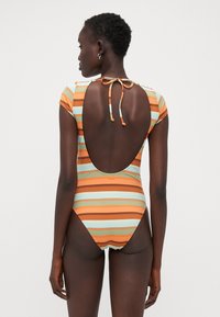 Maillot de bain une pièce à rayures avec un dos ouvert, des manches courtes et un lien de fermeture. Les couleurs incluent l'orange, le teal et le marron. Texture côtelée.