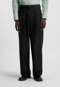 Black pleated trousers with a straight-leg design, made of smooth fabric. Paired with black shoes, worn with a green long-sleeve shirt.