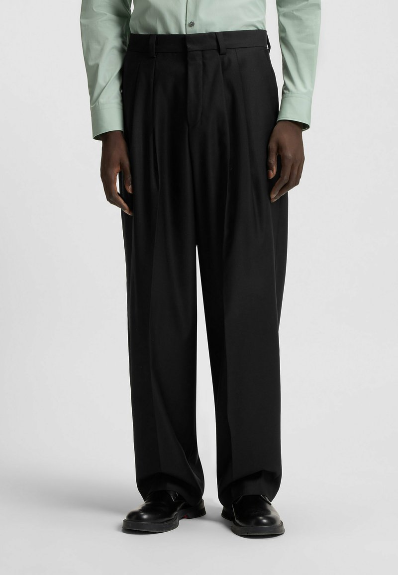 Black pleated trousers with a straight-leg design, made of smooth fabric. Paired with black shoes, worn with a green long-sleeve shirt.