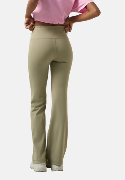 Licht olijfgroene flared broek met een hoge tailleband, gemaakt van rekbaar materiaal. Gladde textuur, zijnaad detail, gecombineerd met lichte schoenen.