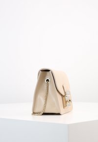 Borsa in pelle beige con forma strutturata, dotata di tracolla a catena, accessori in oro e superficie texturizzata. Patta chiusa con dettaglio a fibbia.