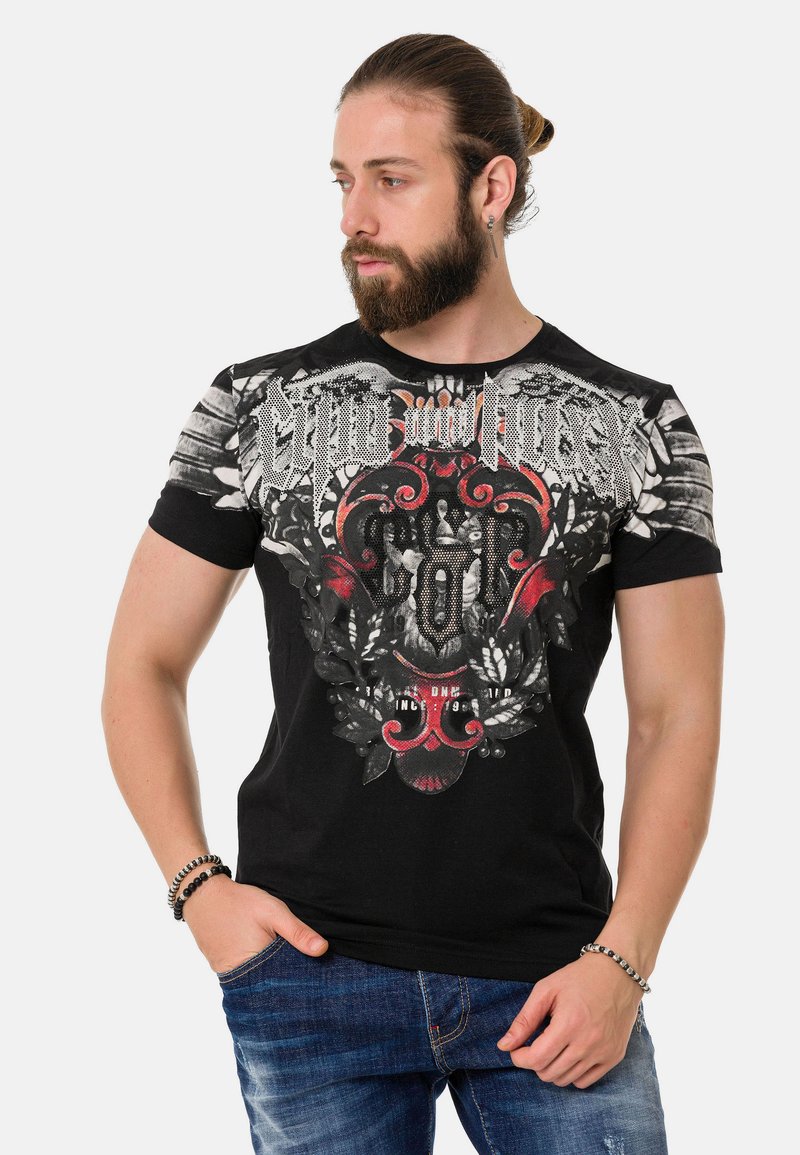 Schwarz T-Shirt mit kurzen Ärmeln und grafischem Design, das rote und weiße Muster, ein Totenkopf und silberne Akzente an den Schultern zeigt.