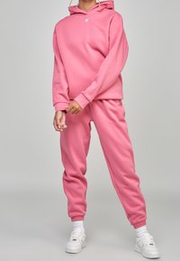 Felpa con cappuccio rosa e pantaloni jogger abbinati realizzati in tessuto morbido; presenta polsini a coste, un logo sul petto e una vita elasticizzata.