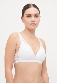 Hvit blonde-bralette med trekantet koppdesign, strukturert stoff og brede stropper. Har delikate blondeakenter på siden.