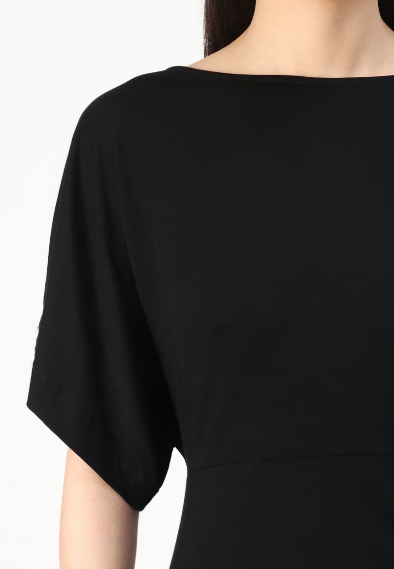Zwarte top van zacht stof, met een brede halslijn en korte vleermuismouwen. Naaddetails op de taille zorgen voor een subtiele vorm.