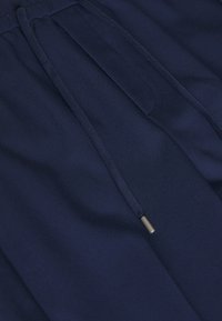 Un pantalon de jogging bleu marine avec une texture douce, doté d'une taille élastique à cordon de serrage et de détails en métal. Aucun poché ni motif visible.