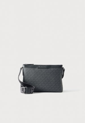Bolso bandolera negro de Michael Kors con un estampado de monograma repetido, cierre superior con cremallera y correa ancha ajustable, sobre un fondo liso.