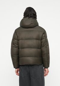 Chaqueta acolchada verde oliva con capucha, con un diseño acolchado y superficie texturizada. Dobladillo ajustable con bolsillos laterales ocultos.