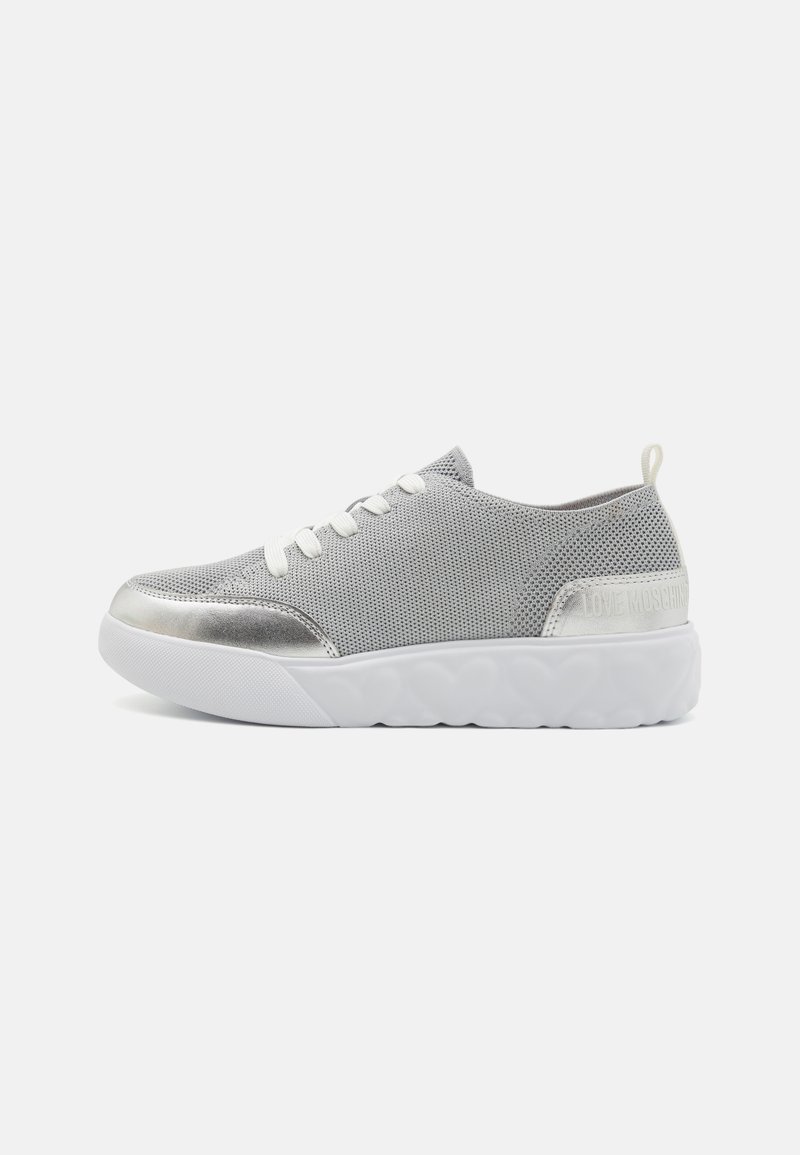Gray mesh sneaker with metallic silver accents, white rubber sole, and matching laces. Features a back pull tab and logo detail.