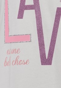 Tissu blanc avec des lettres "LAV" en paillettes roses, agrémenté de clous argentés, avec en dessous un texte en rose en cursive "est une belle chose".