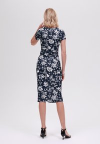 Blomstrete bodycon-kjole med marineblå bakgrunn og hvite blomster, korte ermer, kne-length cut, og svarte høyhælte sko.