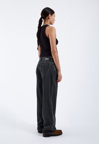Black tank top paired with loose-fitting, dark gray denim jeans. The jeans feature a label on the waistband and straight leg design.