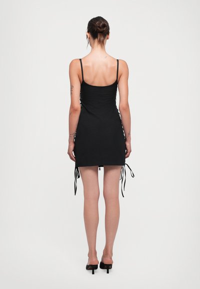 Black ruched mini dress with adjustable side ties, thin straps, and a smooth texture, featuring a fitted silhouette and above-the-knee length.