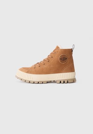 Boots înalte din suede maro cu talpă din cauciuc crem, vârf rotund, cinci orificii pentru șireturi, guler captusit și logo circular pe lateral.