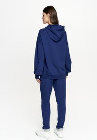 Granatowy zestaw bluzy z kapturem i spodni dresowych z miękkiej tkaniny. Bluza ma kieszeń kangurkę i regulowany sznurek. Prosty design i luźny krój.