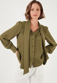 Olive green blouse with a V-neck, button down front, long sleeves with cuffs, and a matching scarf draped over the shoulders. Smooth texture.